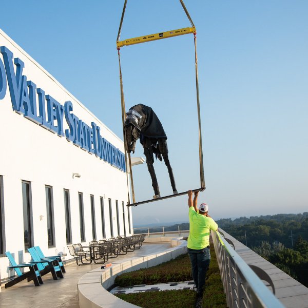 construction workers reach for a sculpture that is hoisted by crane on the terrace of DCIH, Pew Grand Rapids Campus