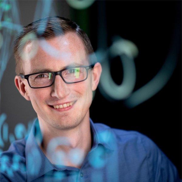 Zachary DeBruine in blue shirt behind screen with coding written on it