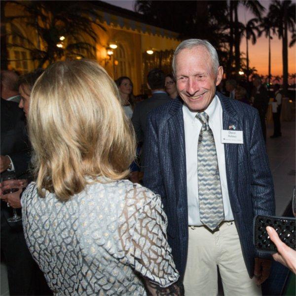 Dave Mehney in open suit jacket standing talking to woman with back to camera