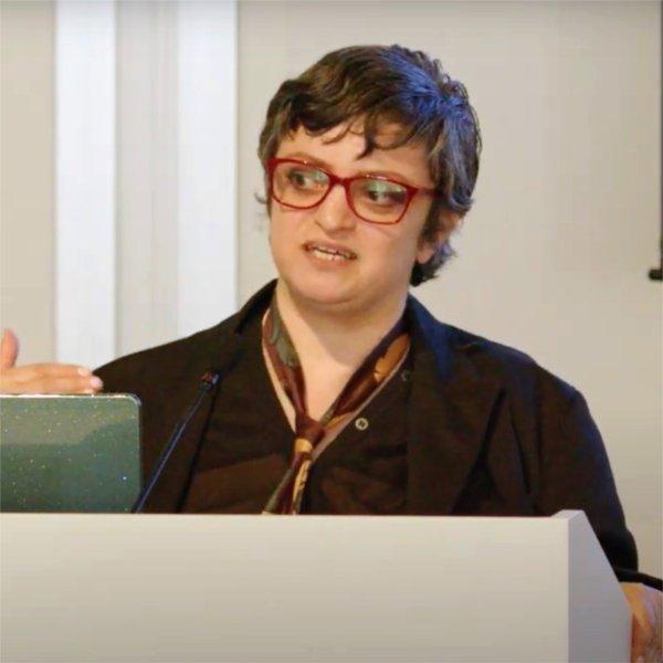 A person standing at a podium gestures while speaking.