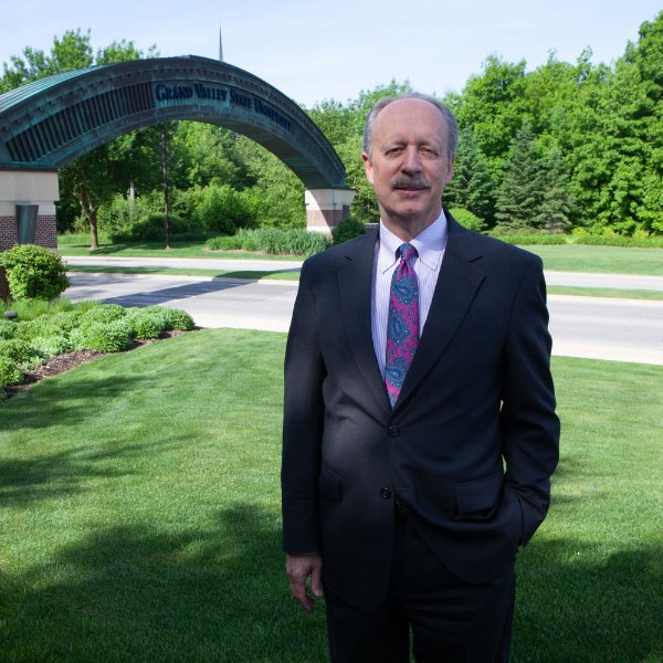 Matt McLogan smiles as he poses in front of the arch at the entrance to Grand Valley State University.