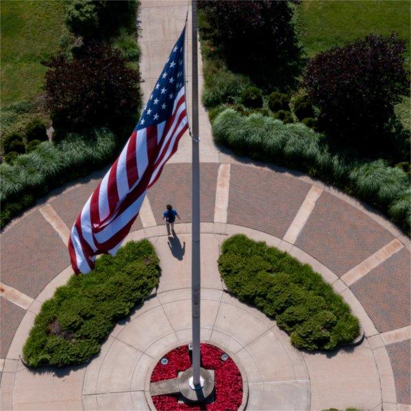 The American flag is seen from above, with a person walking underneath it, on the Grand Valley campus.