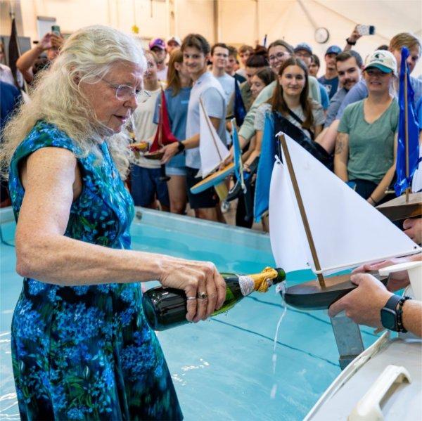 Shirley Fleischmann pours champagne on a model sailboat while standing in a shallow pool