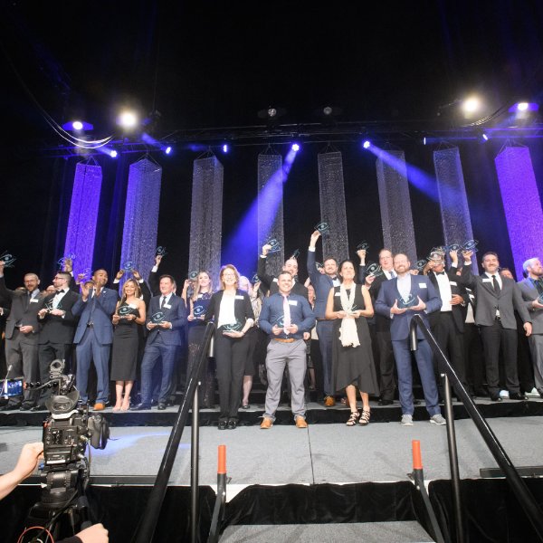large group of people on stage holding awards, blue spotlights in back