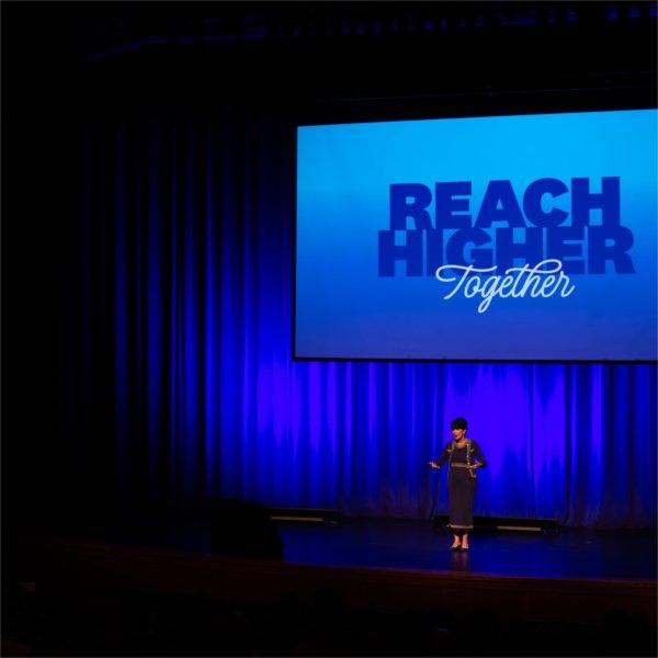 President Mantella on stage, Reach Higher Together on projection screen