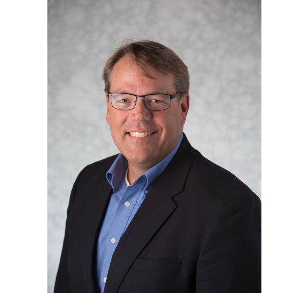 Greg Warsen headshot, he is wearing a dark jacket and blue shirt