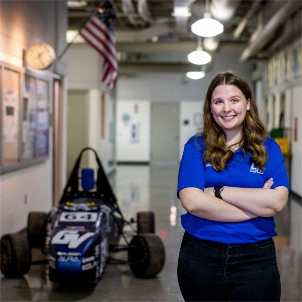 Annika Mattson stands with arms crossed in a hallway with the Laker Racing car on the left