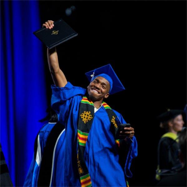 A graduate proudly holds up his diploma as he crosses the stage during Commencement.