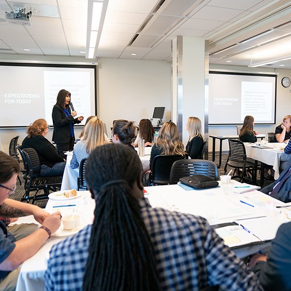 In a 2019 photo, President Mantella stands at the front of a room with a microphone to speak with faculty and staff members who are seated at tables.