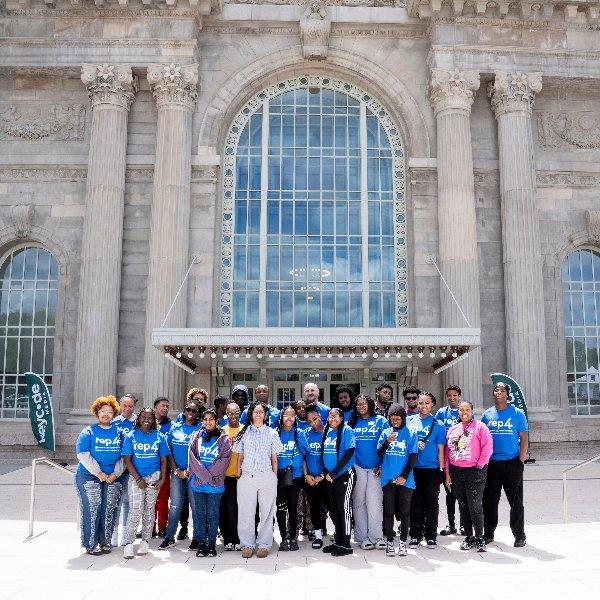 A group of people in blue REP4 shirts stand in front of the ornate entrance of Michigan Central.