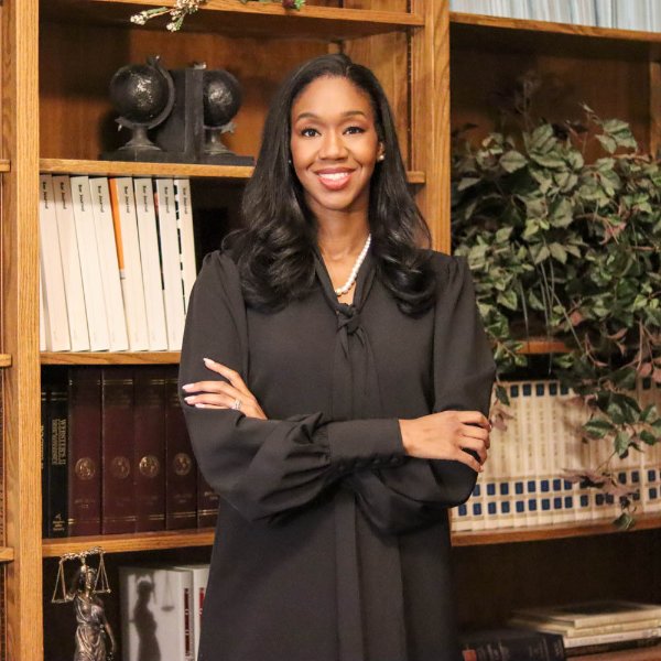 Kyra Harris Bolden stands with arms crossed in front of a bookcase