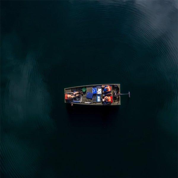 Three AWRI staff members wearing life vests sit in a boat on a lake.