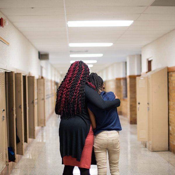 Teacher comforting a student as they walk down a school hallway.