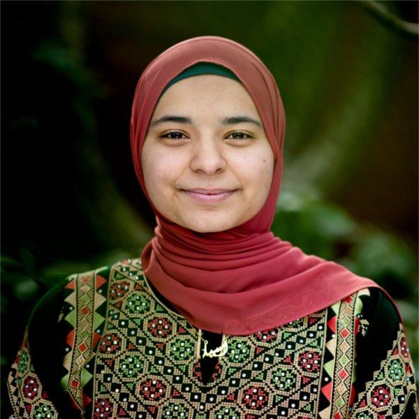 Aseel Ayesh standing outside in a maroon hajib