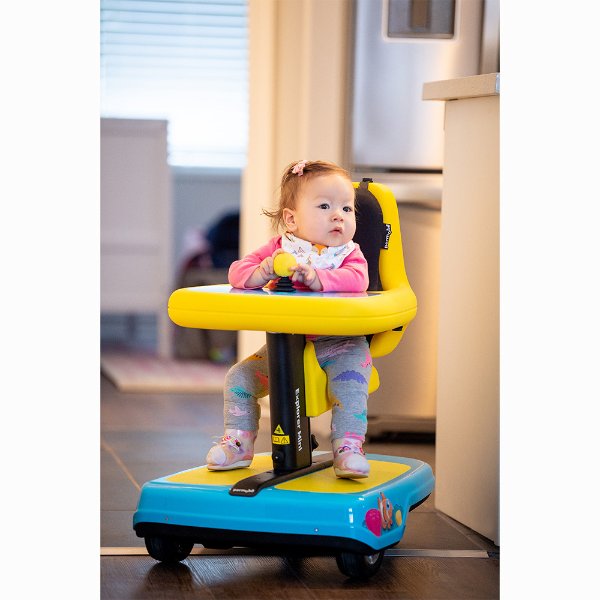 toddler in blue and yellow mobility device pictured inside a home or office setting