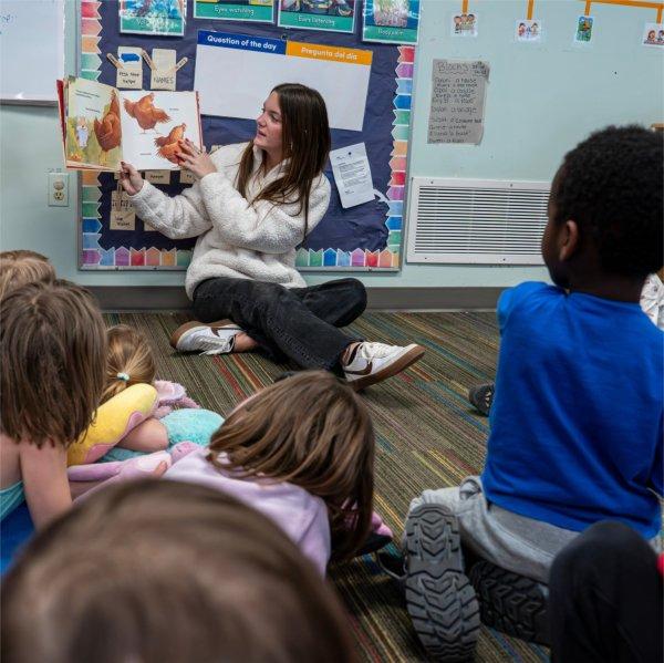 Bailey LoFiego holds a children's book up to a group of young children seated on the floor