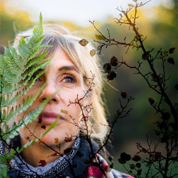 A person looks into the distance with a leaf and some brown branches in the foreground.