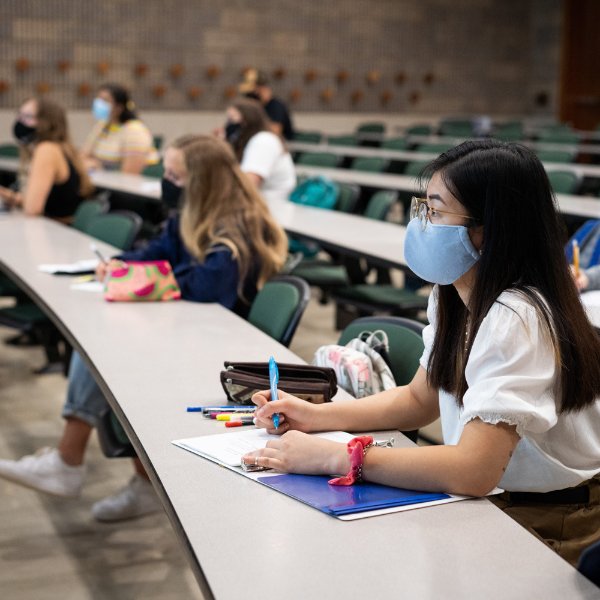 Students are pictured in class, taking notes and wearing masks