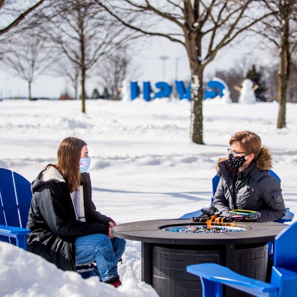 two students wearing masks talking outside at fire pit