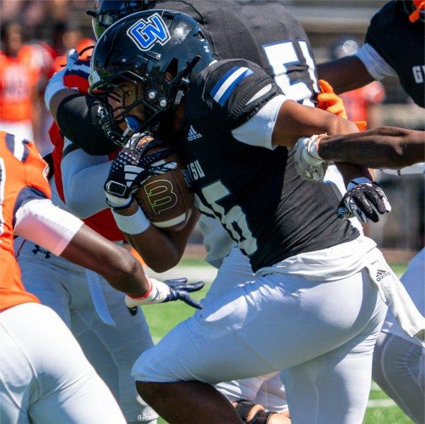 A football player carrying the football runs past opponents.