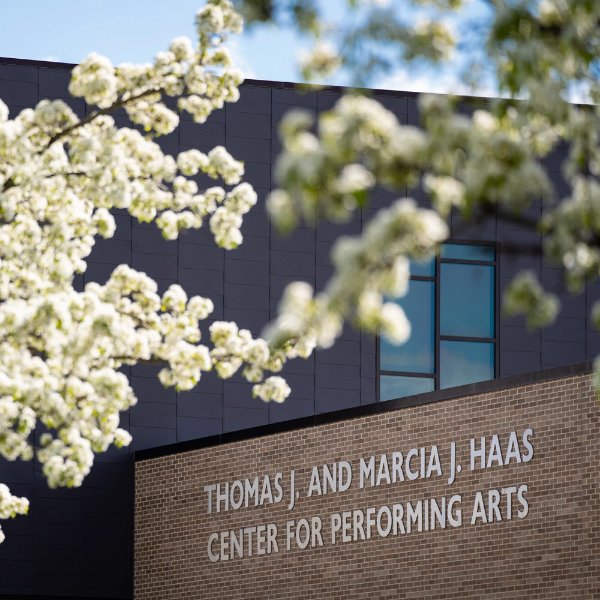 The building name on the outside of the Thomas J. and Marcia J. Haas Center for Performing Arts is framed by white flowers.
