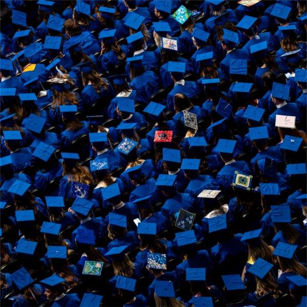 A group of people wearing blue graduation caps, some decorated colorfully, is seen from above.