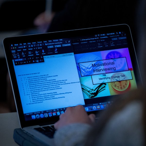 A computer screen shows a graphic with boxes containing the words "motivational interviewing" and "identifying change talk." Text on the left is small and indecipherable.