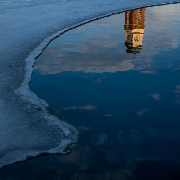 Carillon Tower reflected in Zumberge Pond water, with a curve of ice on the left side.