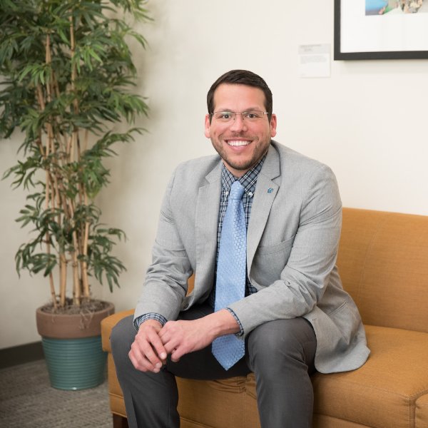 Jesse Bernal sitting on a coach wearing a gray suit with blue tie
