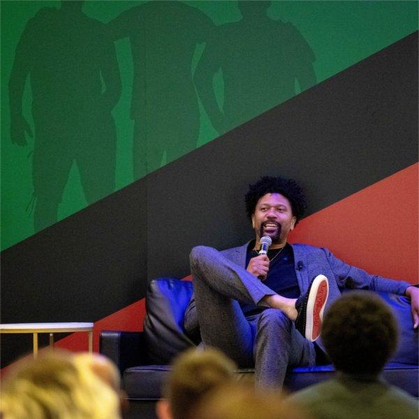 Jalen Rose sits in a chair with a microphone in front of banner