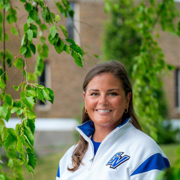 Colleen Bailey wears a white and blue GV quarter zip and stands beneath a tree in front of Kistler Living Center.