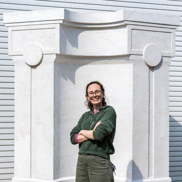 Gabrielle Egnater pictured in front of her sculpture, a white pillar in front of a white garage door