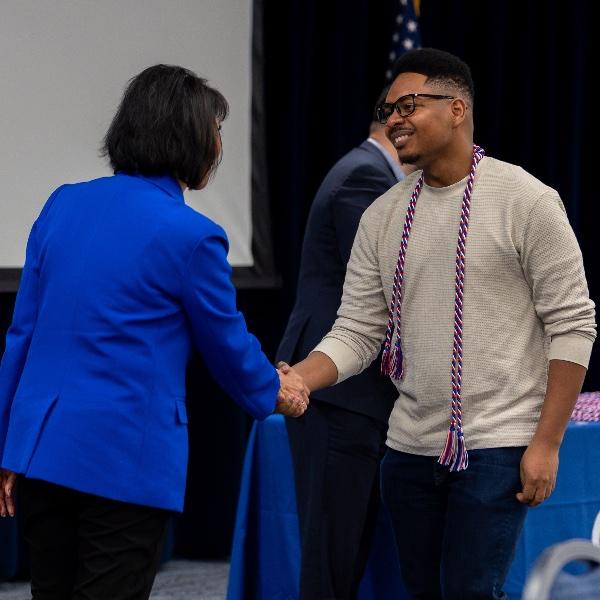 President Mantella shaking hands with a student veteran wearing his cords.