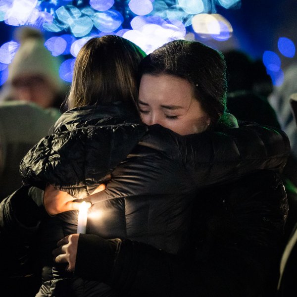 Two students hug at the vigil while holding electric candles.