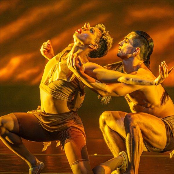 Two people dance dramatically with one looking upward with arms extended.