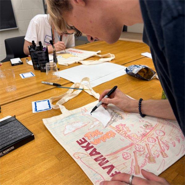 A person uses a marker on a drawing that includes the words "the voyage" and #vmake