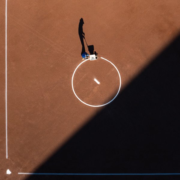A worker draws a chalk circle around the pitching rubber on a ball field.
