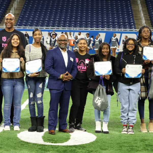 VP Truss is pictured on a football field (Ford Field) with youth holding certificates and a man in the background