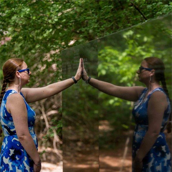 A person places their hand on a stone wall. Their reflection is seen to the right.