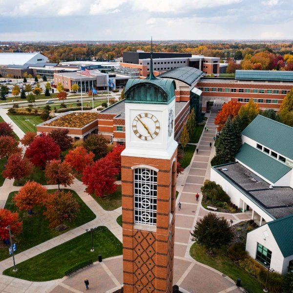 A carillon is shown in the foreground with buildings and people on walkways in the background.