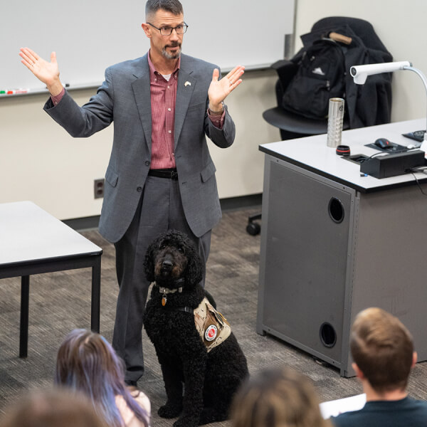 man at front of classroom, service dog at his feet