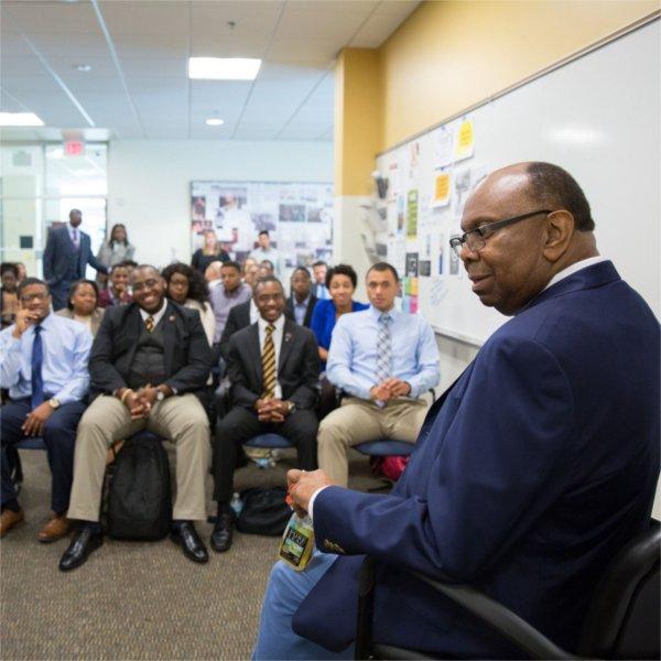 William Pickard at left seated in chair, rows of students listening in the Multicultural Affairs office