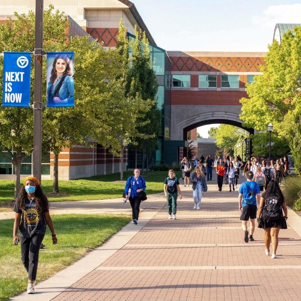students walking on Allendale Campus; banner hanging from lightpost reads Next is Now