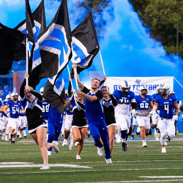 Cheerleaders lead football team out on to field at start of game.