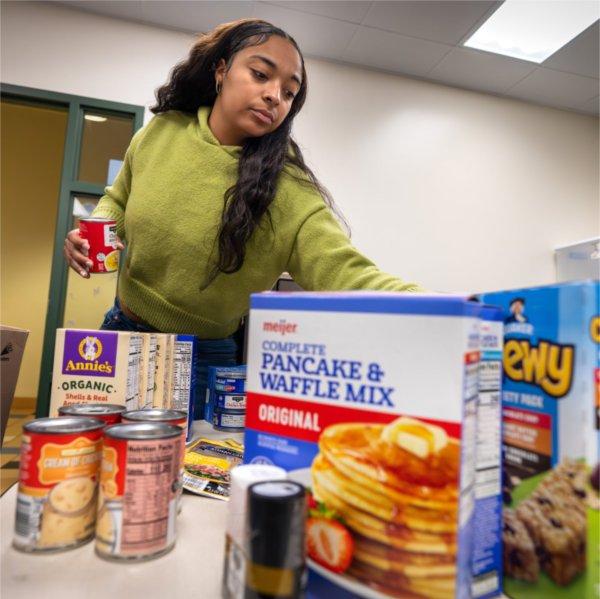 A young woman organizes a box of dry goods received by Replenish.