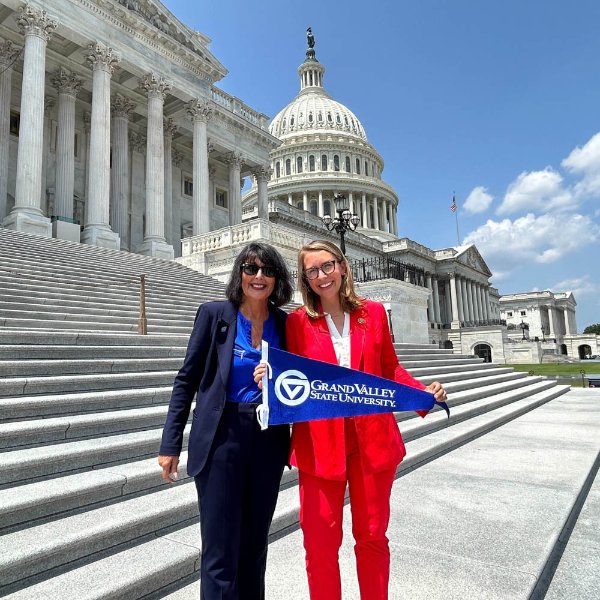 President Mantella and Representative Hillary Scholten stand on the Capitol steps together and hold a GVSU flag.