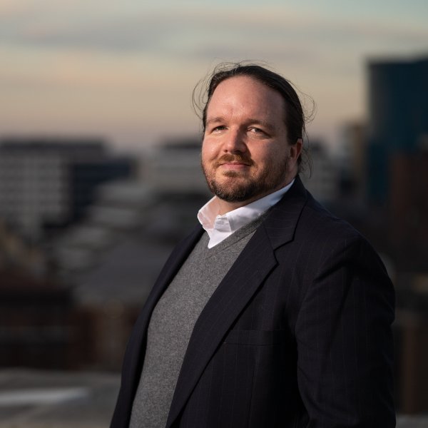 A person smiles while looking at the camera with part of the City of Grand Rapids skyline in the background.