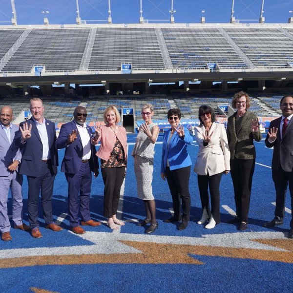 President Mantella and other rep 4 leaders pose for a photo on a blue football field. They all hold 4 fingers up.