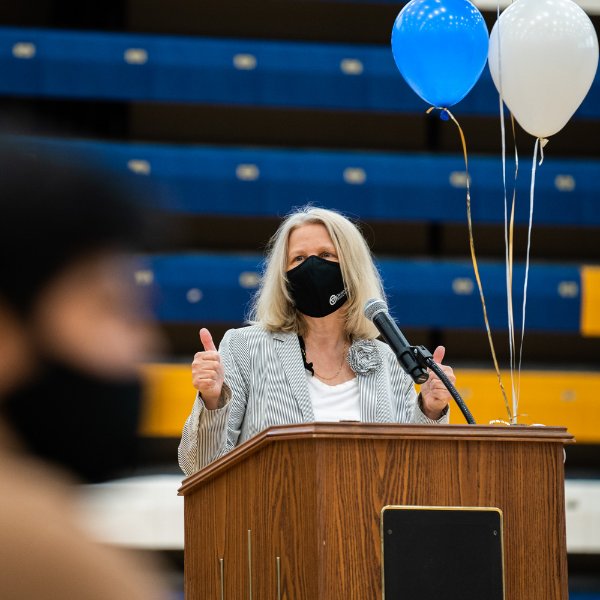 Jean Nagelkerk, with mask on, at podium giving two thumbs up