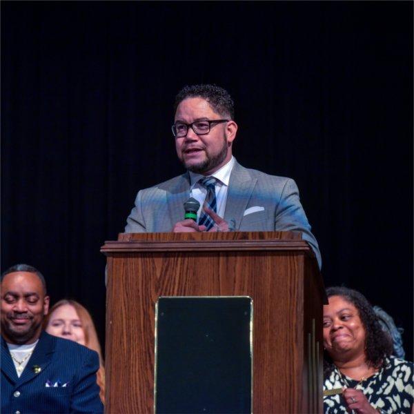 Danny Velez at podium, people in chairs behind him.